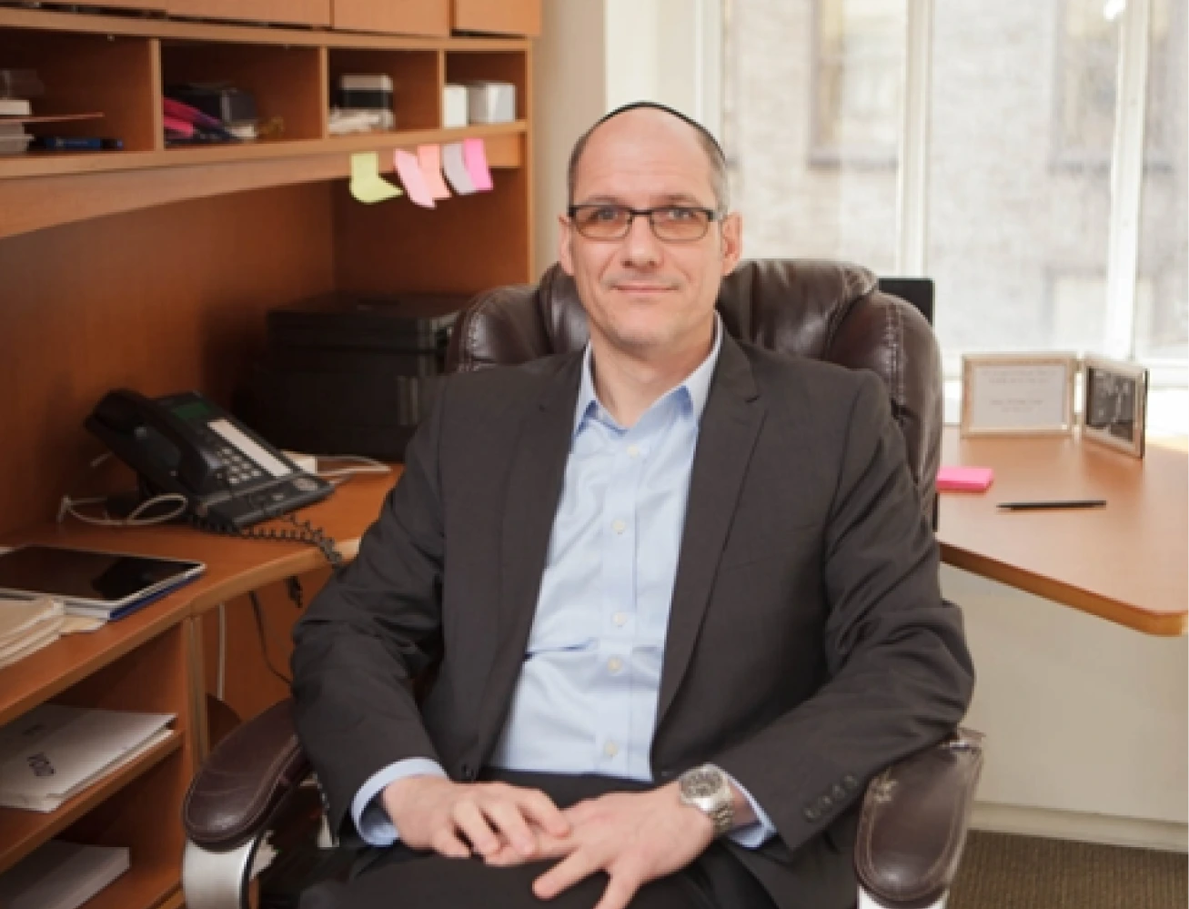 Alfredo Nudman seated at his desk in a professional office with wood cabinetry and shelving